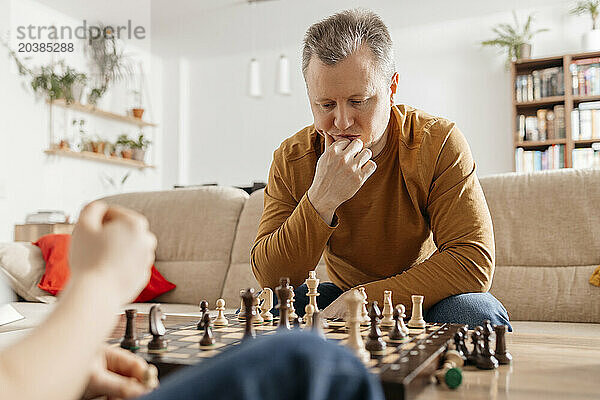 Thoughtful man looking at chess pieces in living room