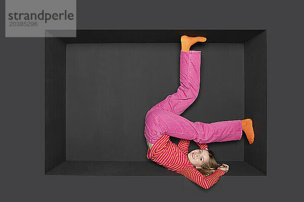 Smiling teenager with legs up inside alcove by black background