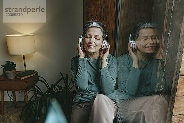 Woman listening to music sitting near glass window at home