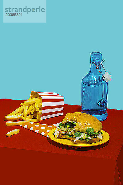 Cheeseburger with french fries near soda bottle on table against blue background