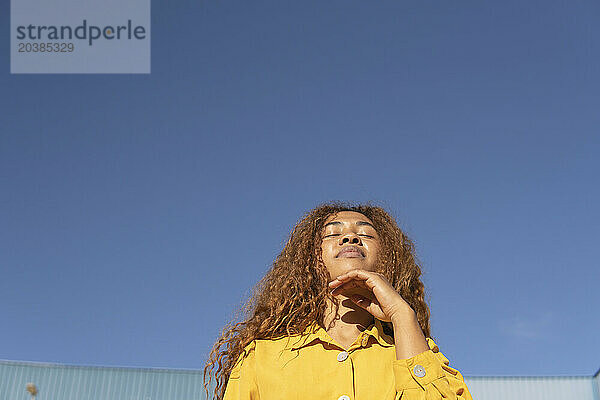 Young woman with hand on chin under clear blue sky