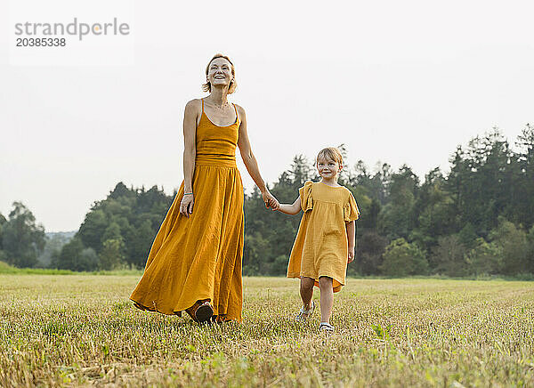 Mother and daughter holding hands and walking in meadow