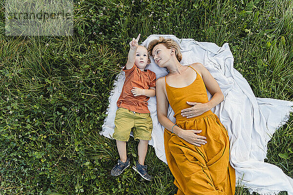 Mother and son lying on blanket over grass in meadow