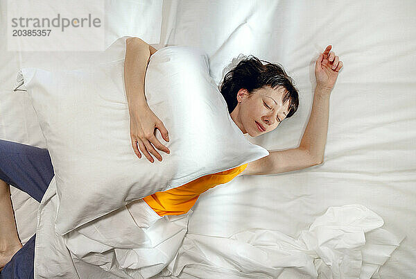 Woman sleeping with pillow on bed at home