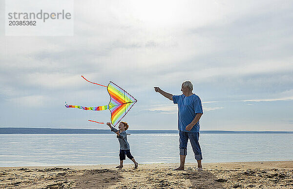 Senior man and grandson flying kite near sea at beach