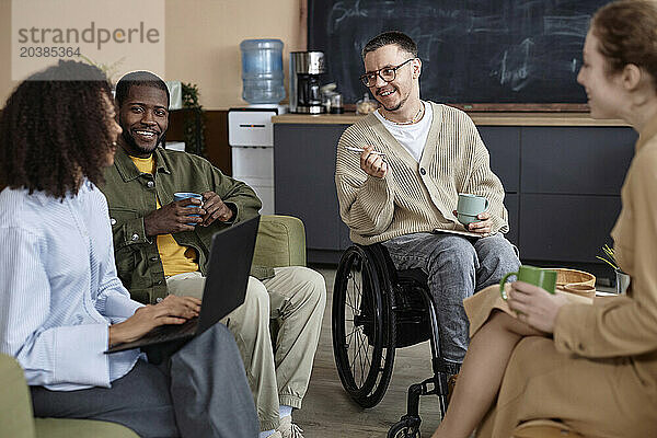 Smiling business people siting with coffee cups and having discussion in office