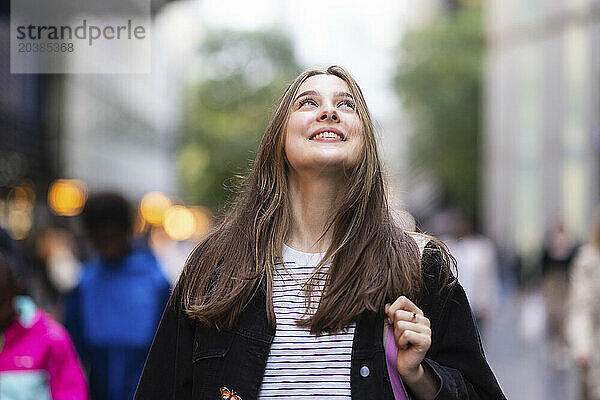 Smiling young woman with long hair looking up in city