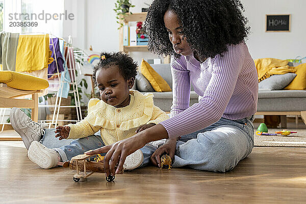 Mother and daughter playing toy airplane sitting on floor at home