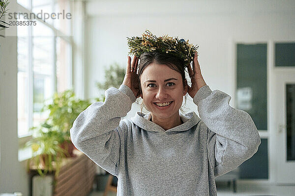 Happy woman wearing flowers on head at home