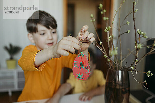 Boy decorating cardboard Easter eggs on twig
