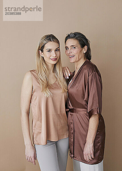 Smiling woman standing with daughter against beige background