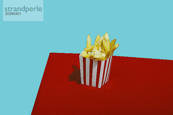 French fries in container on table against blue background