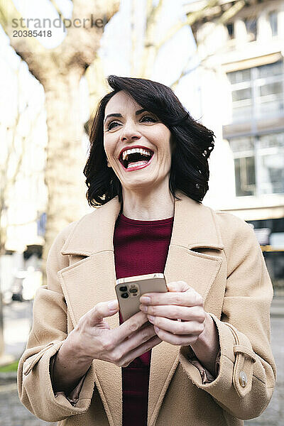 Happy mature businesswoman wearing overcoat using smart phone