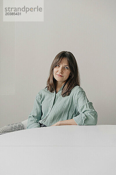 Smiling woman sitting near table in front of wall