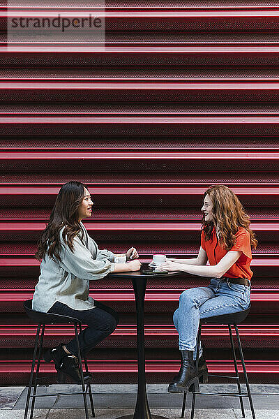 Friends talking to each other sitting near shutter at sidewalk cafe