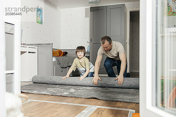 Boy helping father in unrolling carpet on floor at home