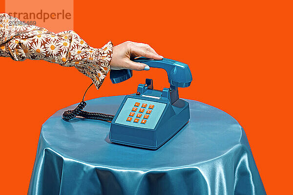 Woman picking up telephone receiver on table against orange background