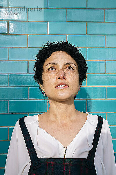 Thoughtful woman standing in front of blue brick wall