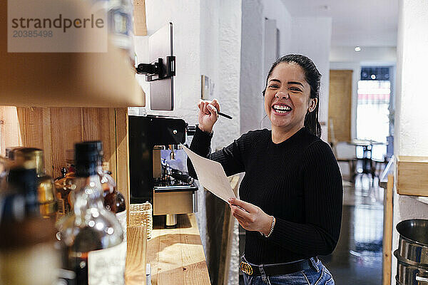 Cheerful restaurant owner standing with document in illuminated kitchen