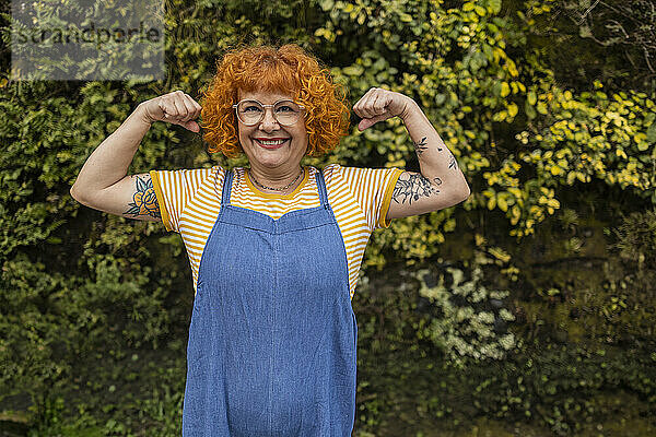 Smiling redhead senior woman flexing muscles