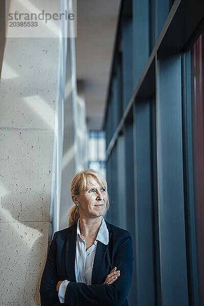 Thoughtful businesswoman standing with arms crossed near column