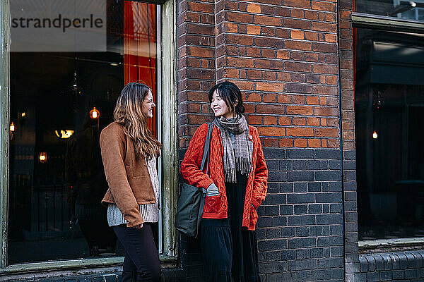 Happy sisters standing and talking near wall