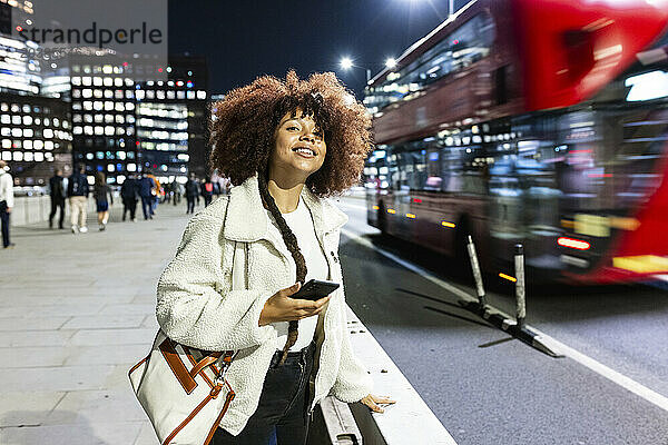 Happy young woman standing with mobile phone on road in London City