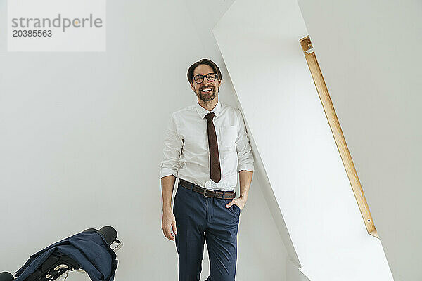 Smiling businessman leaning on white wall with hand in pocket at office