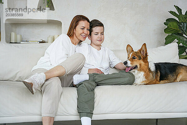 Happy woman and son sitting with dog on couch at home