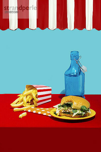 Chicken burger with french fries near soda bottle on table against blue background