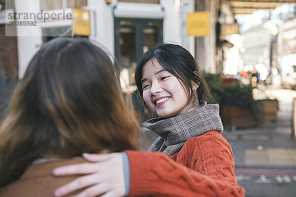 Smiling young woman talking to sister on street