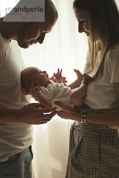 Smiling mother holding baby boy near father at home