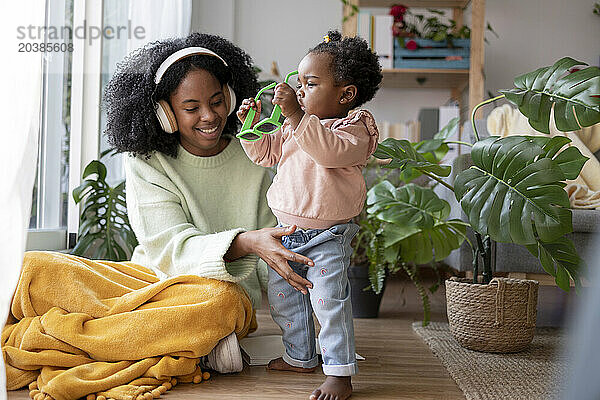 Smiling mother listening to music sitting by daughter with sunglasses at home