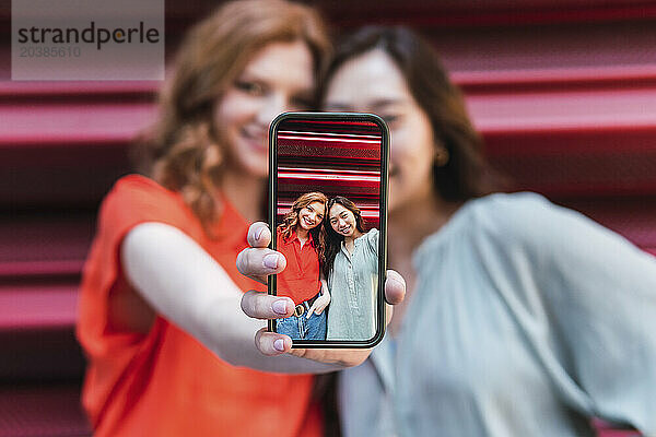 Friends talking selfie through smart phone near shutter