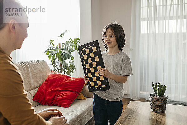 Smiling boy asking father to play chess at home