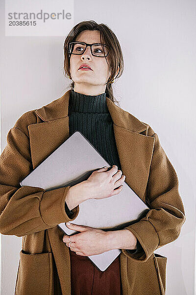 Young businesswoman standing with laptop in front of wall at office