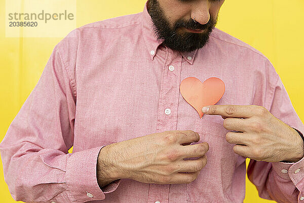 Man with red heart over pink shirt against yellow background
