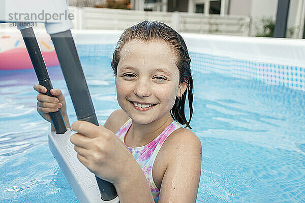 Smiling girl holding ladder in swimming pool