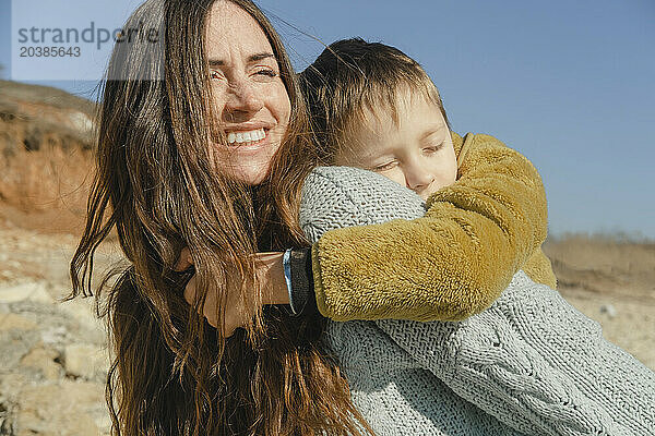 Happy woman giving piggyback to son at sunny day