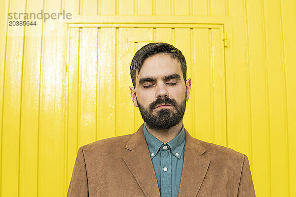 Man with eyes closed in front of yellow wall