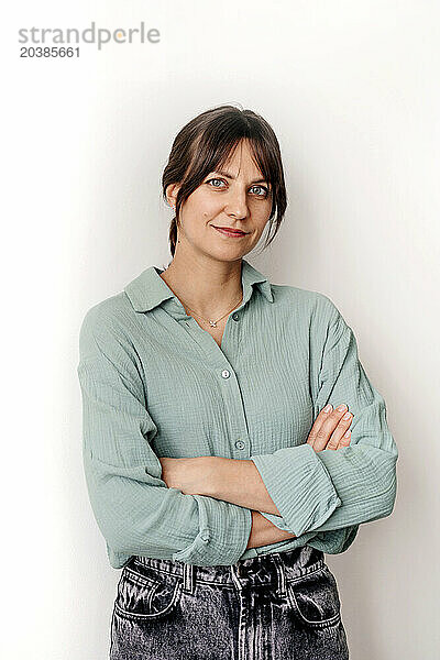 Smiling woman with arms crossed in front of wall