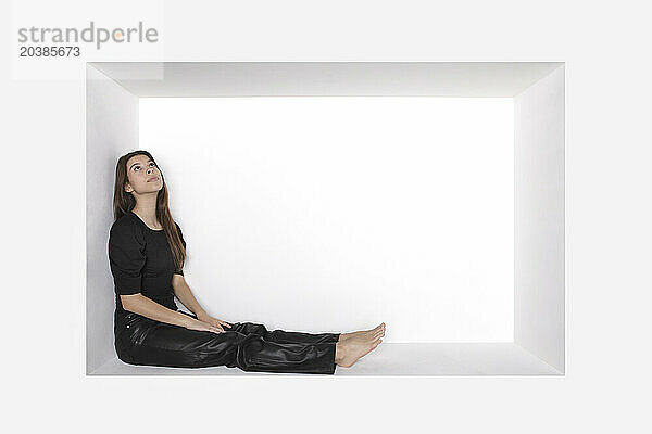 Contemplative girl sitting in alcove over white background