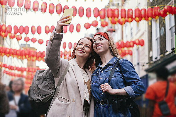 Smiling friends taking selfie under hanging Chinese Lanterns in city