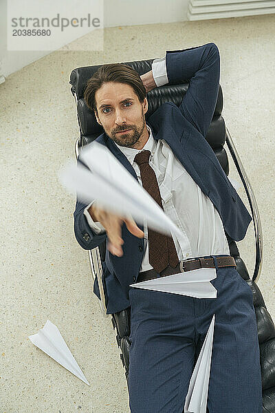 Businessman throwing paper airplane reclining on lounge chair in office