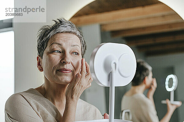 Woman applying face cream looking in mirror