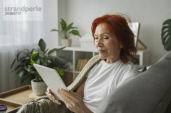 Retired senior woman with digital tablet sitting on sofa at home