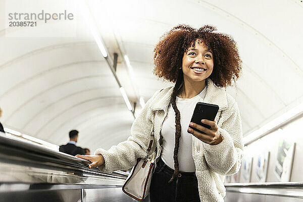 Happy woman with mobile phone on subway escalator