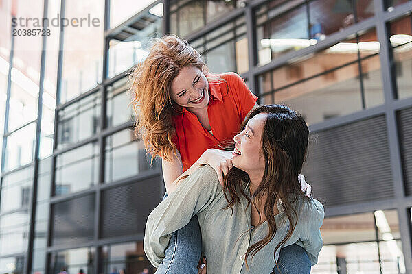 Young woman piggybacking friend in front of building