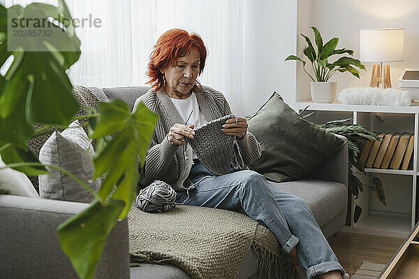 Senior redhead woman sitting on couch knitting at home