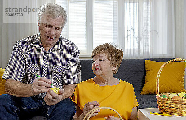 Elderly couple painting eggs for Easter celebration at home